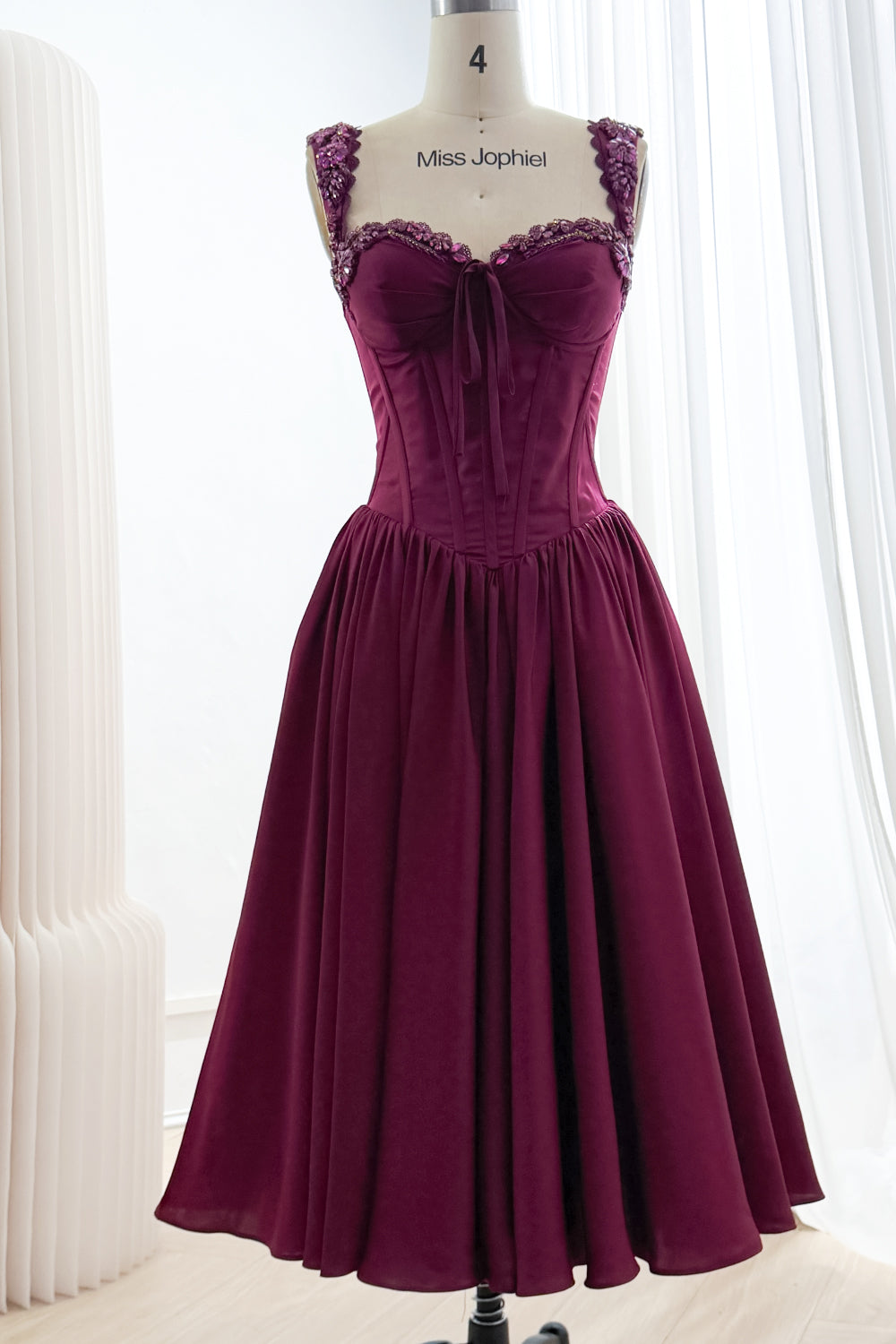 Front view of plum tea-length dress with sparkling sweetheart neckline, front bow, basque waist, and gathered A-line skirt.