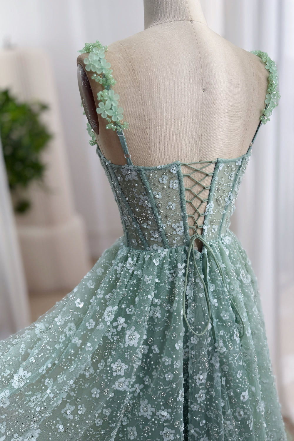 Close-up back view of a sage green floral corset dress with adjustable shoulder straps and lace-up closure