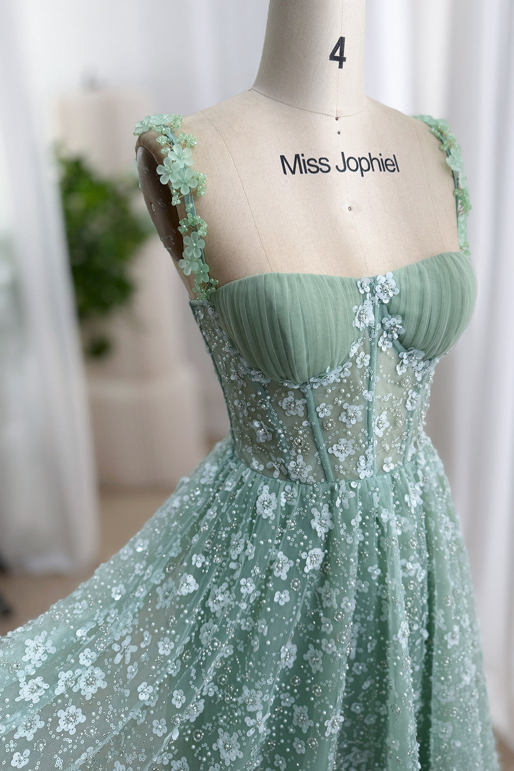 Close-up of a sage green corset dress with gathered tulle cups, floral straps, sequins, and beaded flower appliqués