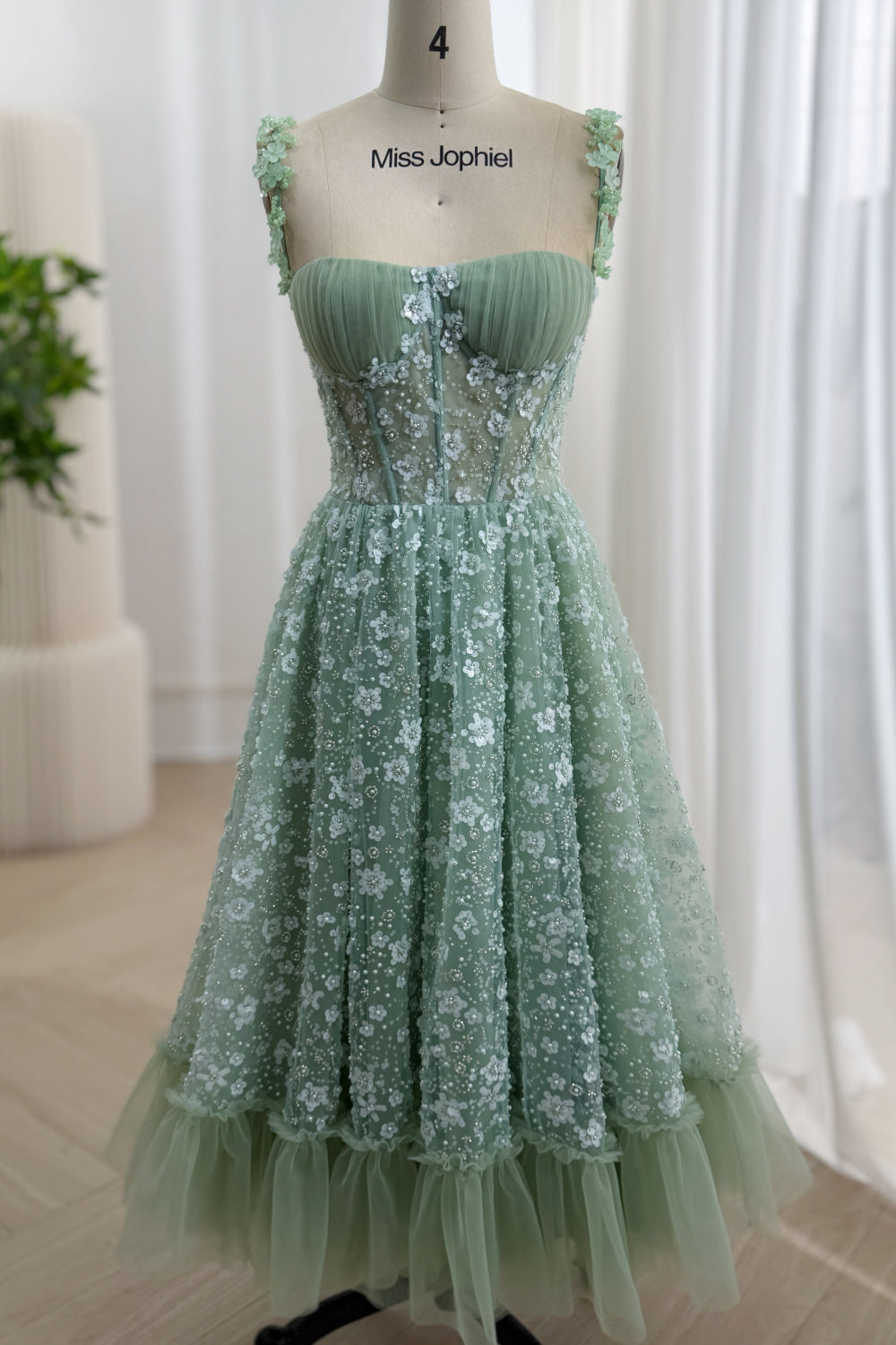 Full front view of a sage green tea-length A-line dress with floral sequin tulle and a ruffled hem