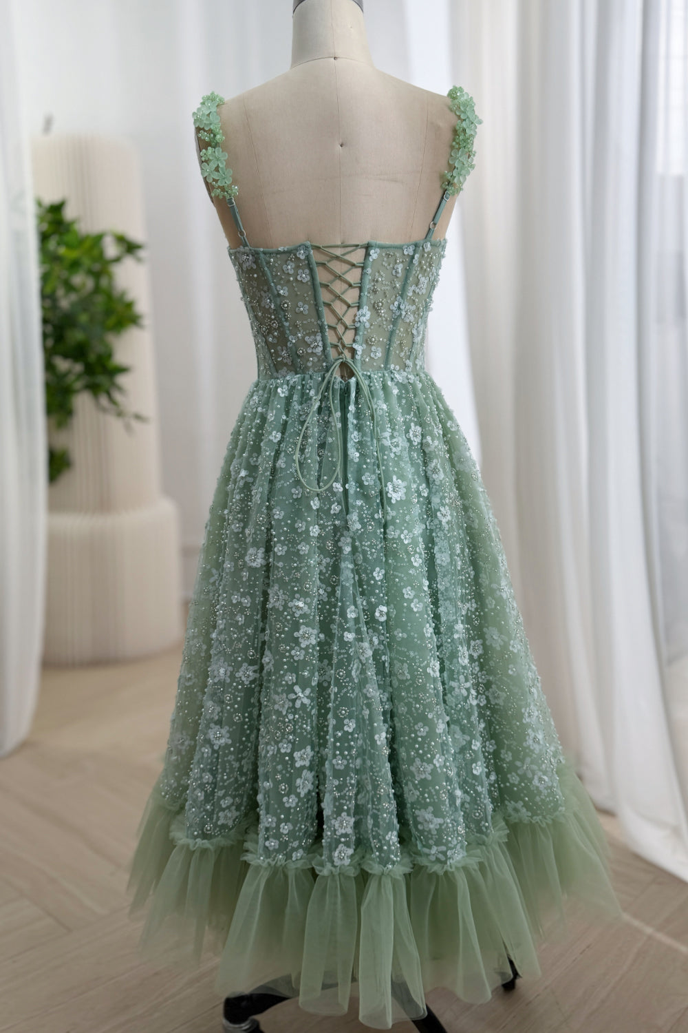 Full back view of a sage green tea-length floral sequin dress with an open lace-up corset back