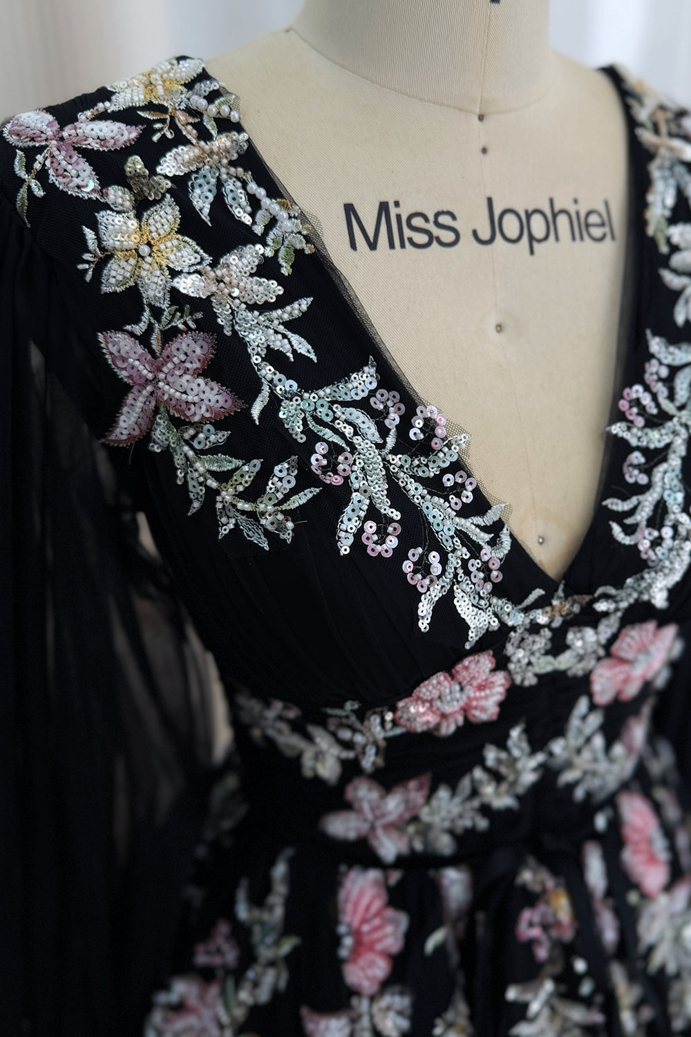 Detailed view of pink, white, gold, and silver sequin floral embroidery along the V-neckline of the black gown
