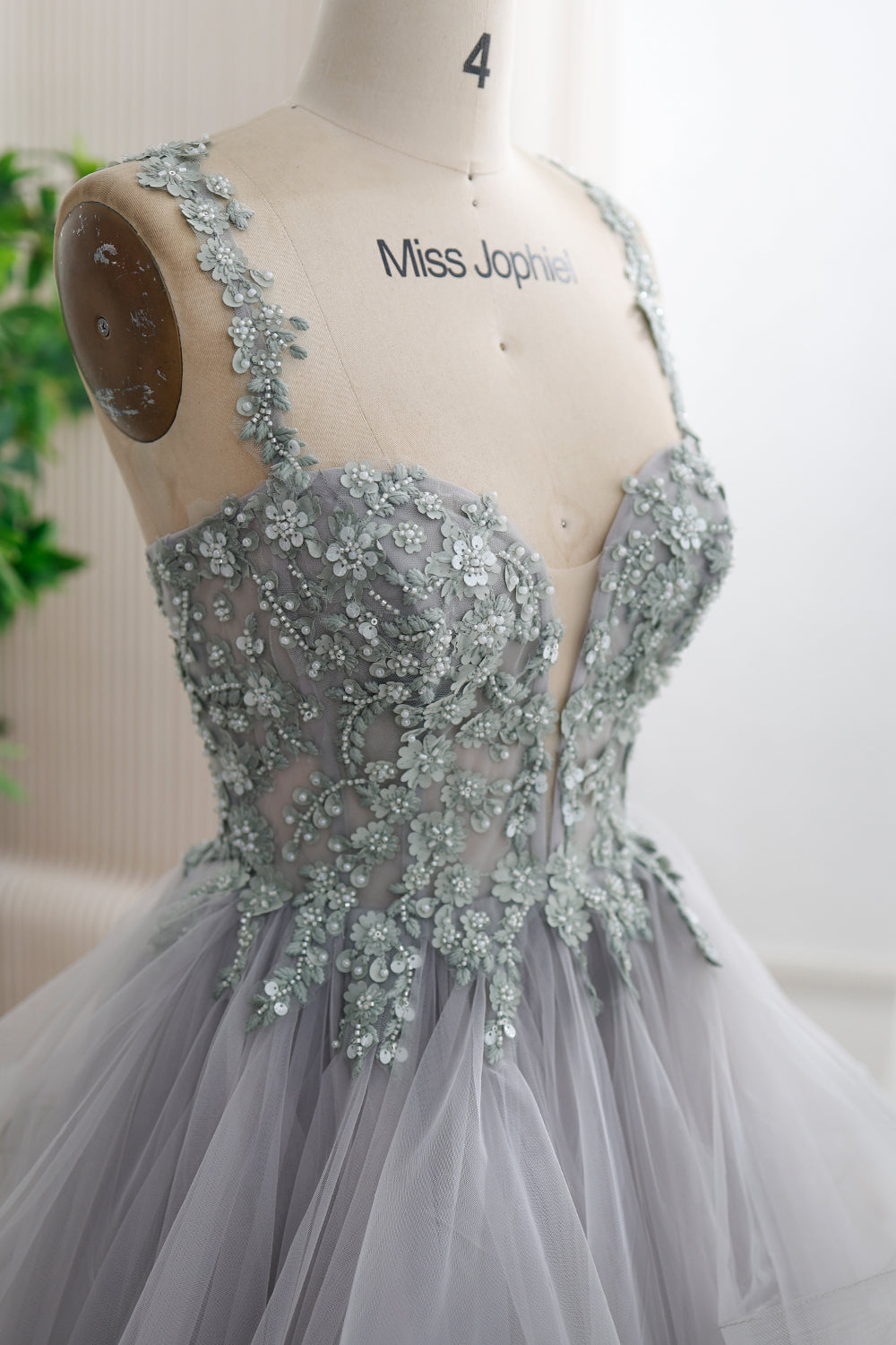 Close-up of floral appliqués, embroidery, beads, and sequins on the silver-gray corset bodice and straps, with a sheer neckline inset.