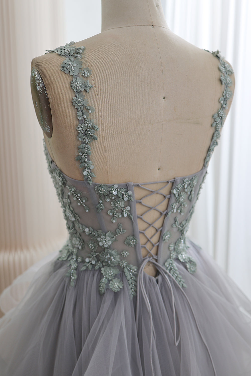 Back bodice detail showing floral embellished straps, sheer embroidered panels, and a crisscross lace-up closure on a silver-gray gown.