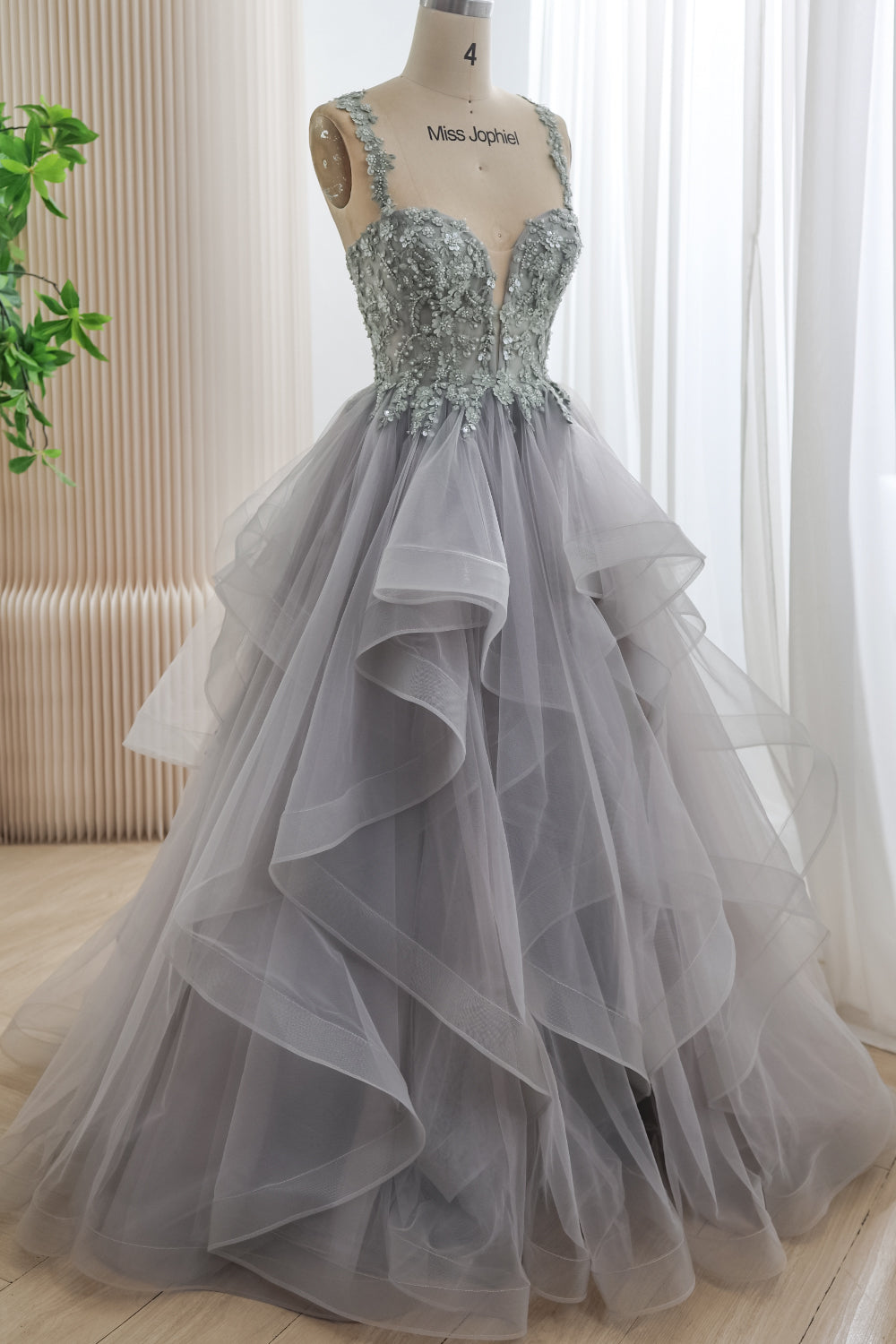 Angled front view of a silver-gray floral corset gown with embellished shoulder straps and a full floor-length tulle ruffle skirt.