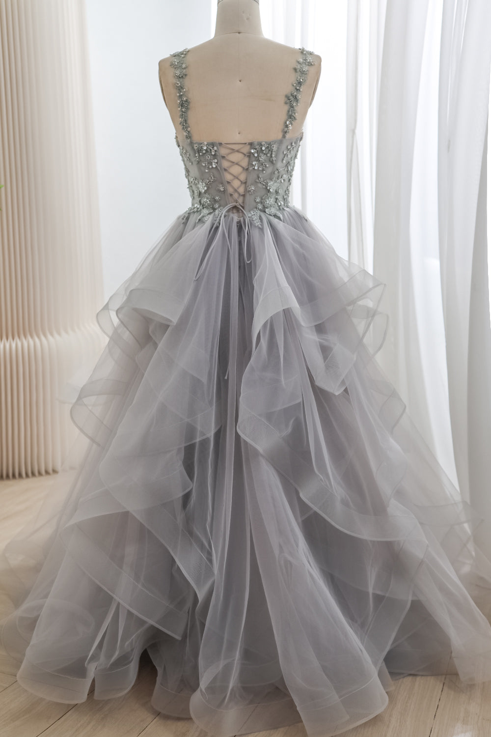 Full back view of a silver-gray tulle ball gown with floral shoulder straps, a lace-up bodice, and cascading floor-length ruffles.