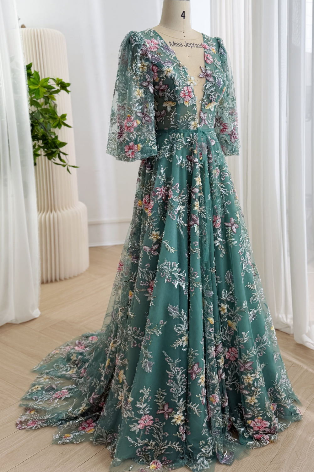 Three-quarter side view of a teal floral embroidered formal gown with sheer sleeves, a full floor-length skirt, and train