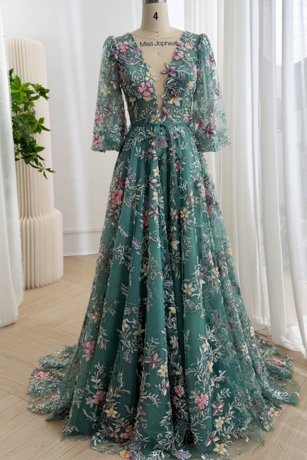 Full front view of a teal floral embroidered tulle formal gown with three-quarter sleeves, an A-line skirt, and a chapel train
