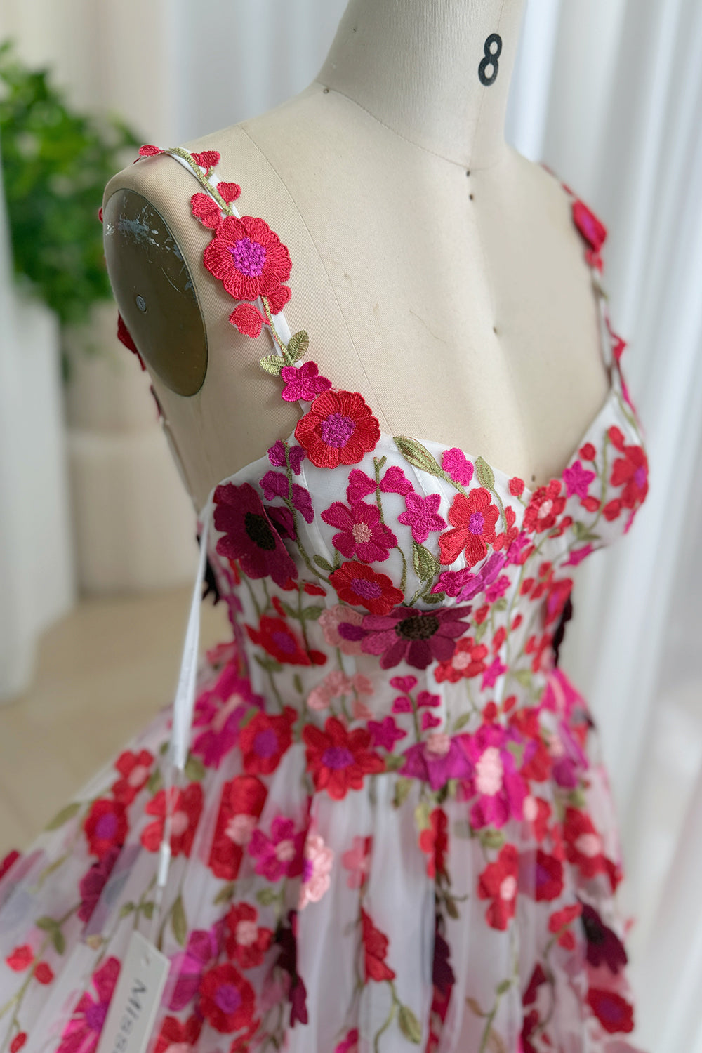 Close-up of colorful floral embroidery and embroidered shoulder strap on white formal dress