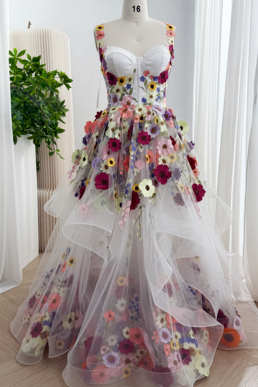 Front view of white floor-length tulle ball gown with multicolor floral appliqués and a layered ruffled skirt