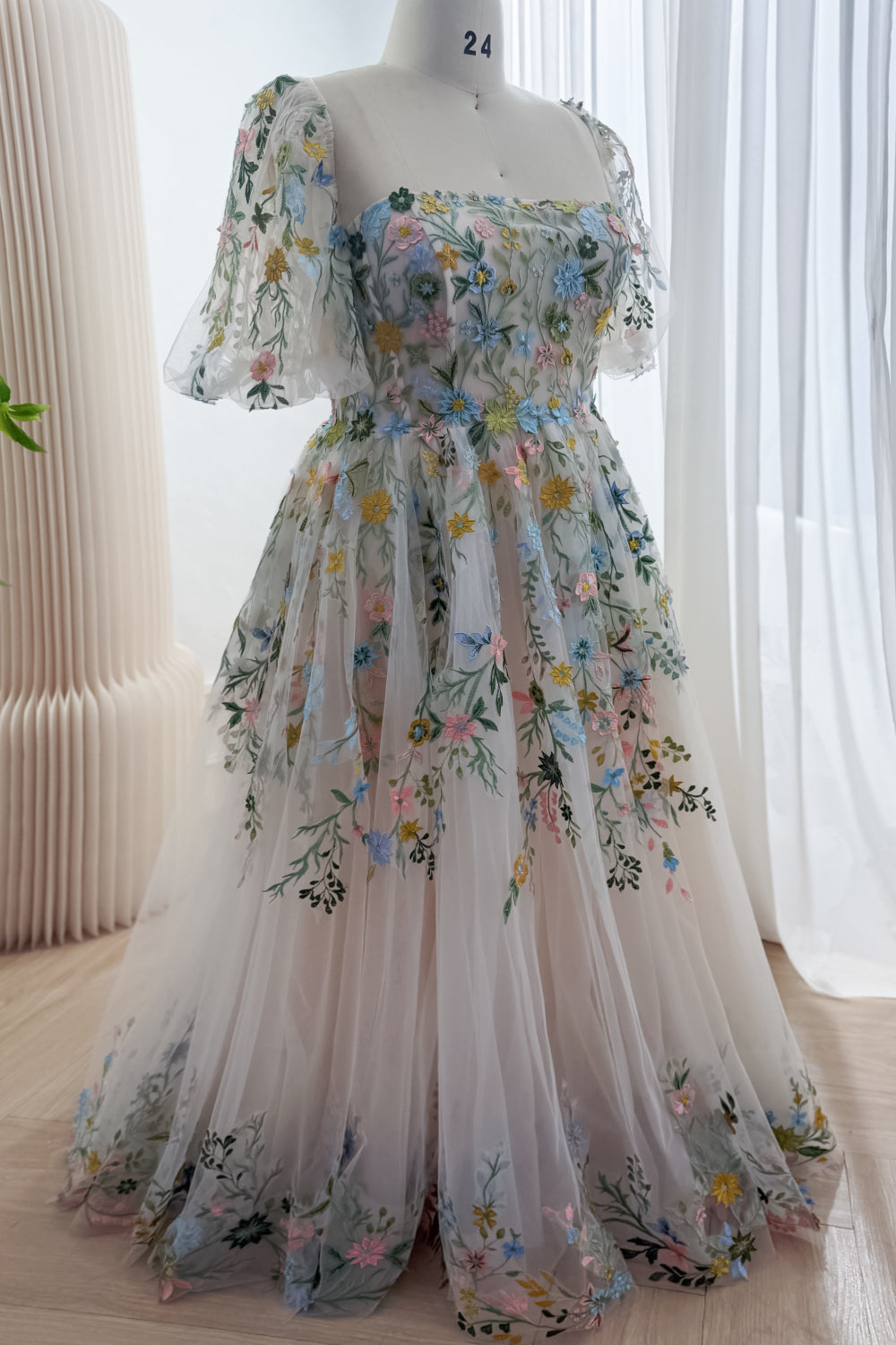 Angled front view of a wildflower embroidered A-line gown with short puff sleeves and colorful blossoms over a pale blush base.