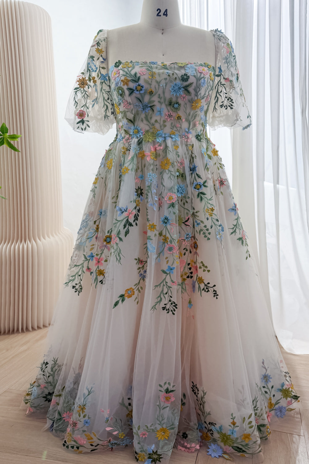 Front view of a pale blush wildflower embroidered tulle gown with a square neckline, sheer puff sleeves and floor-length A-line skirt.