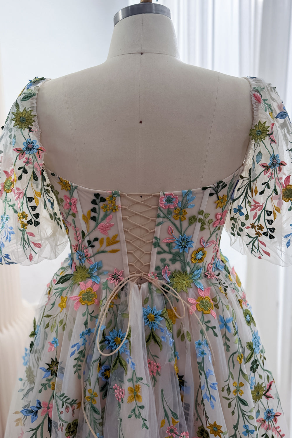 Close-up of the floral embroidered corset back with crisscross lacing, a blush fabric panel and sheer short sleeves.