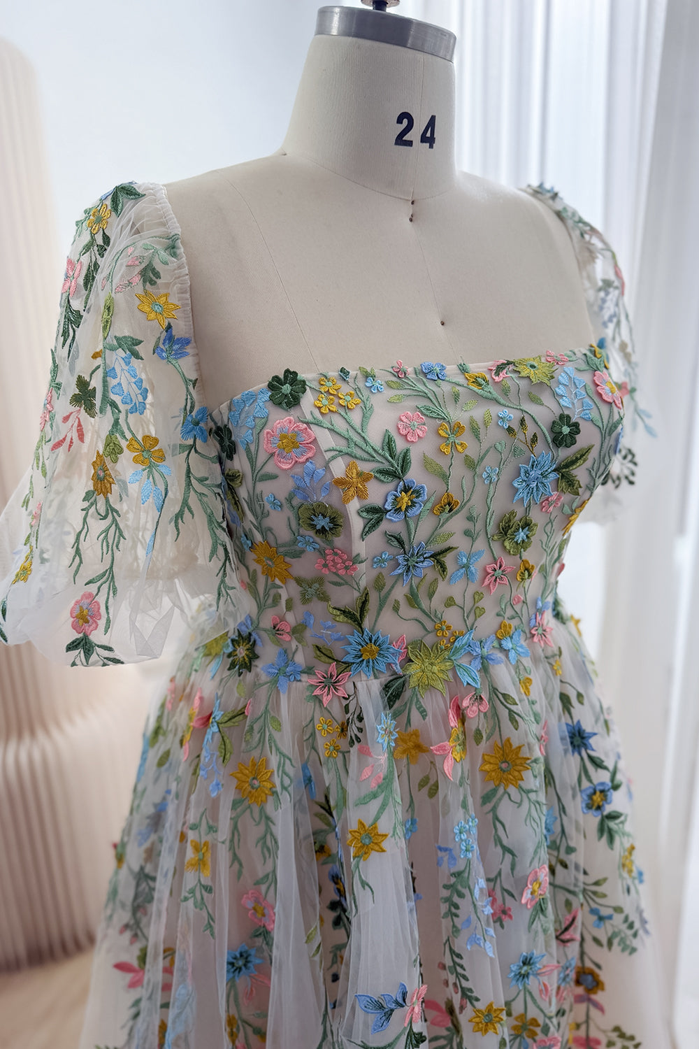 Close-up of the square neckline and sheer puff sleeve with blue, pink and yellow floral embroidery on the fitted bodice.